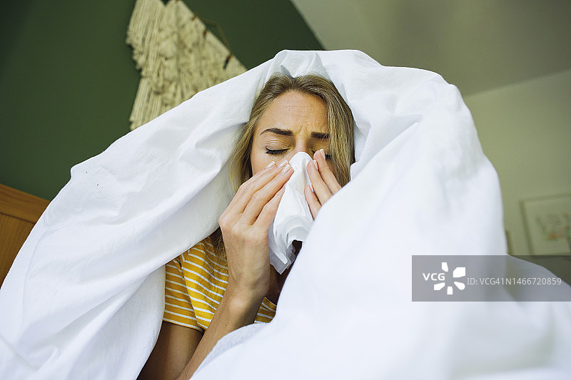 在床上用毯子盖着身体擦鼻涕的女人图片素材