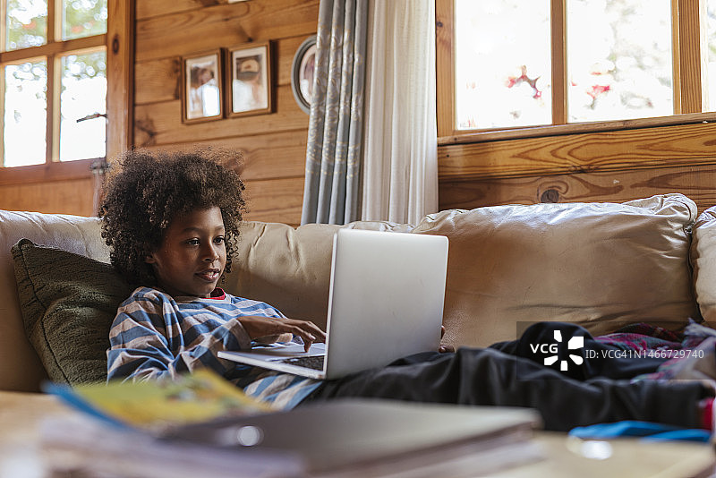 男孩在家靠在沙发上使用笔记本电脑图片素材