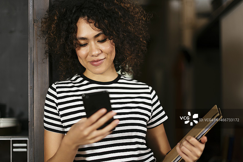 靠在门口使用智能手机的微笑自由职业者图片素材