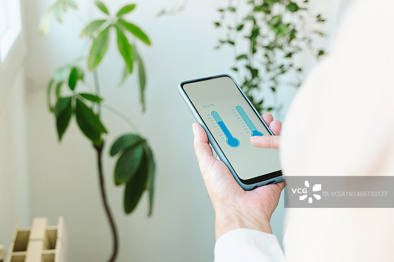 特写：女人在家用智能手机屏幕调节暖气温度图片素材