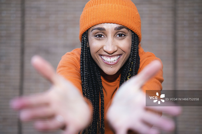 快乐的女人戴着橙色针织帽在墙前做手势图片素材