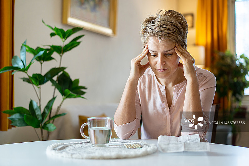 一位忧虑的女人用手指按着太阳穴，盯着她的激素替代疗法药丸图片素材