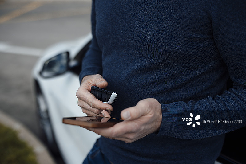 手持车钥匙使用手机的男人图片素材