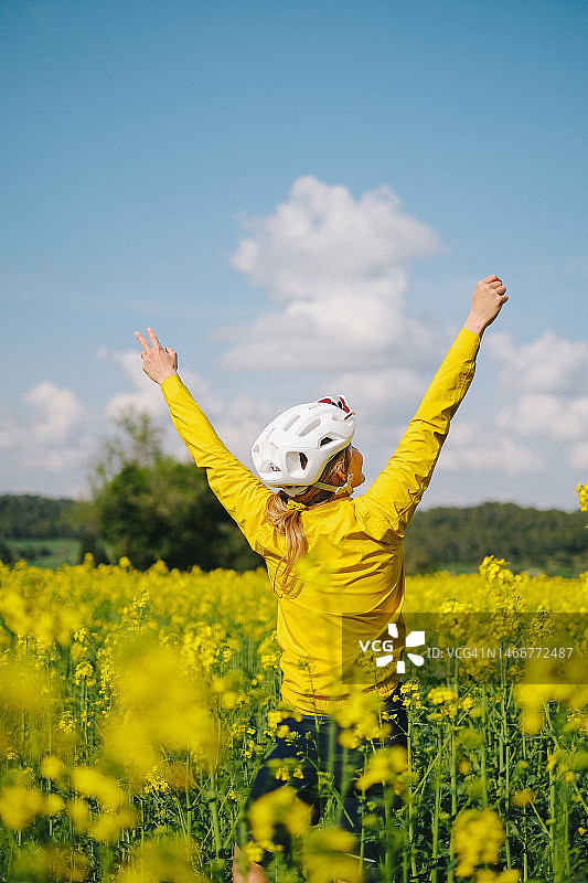 年轻女子在油菜籽田中停下公路自行车图片素材