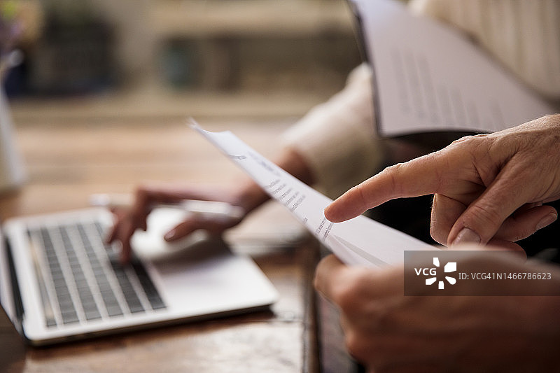 妇女在笔记本电脑旁审阅纸质文件图片素材