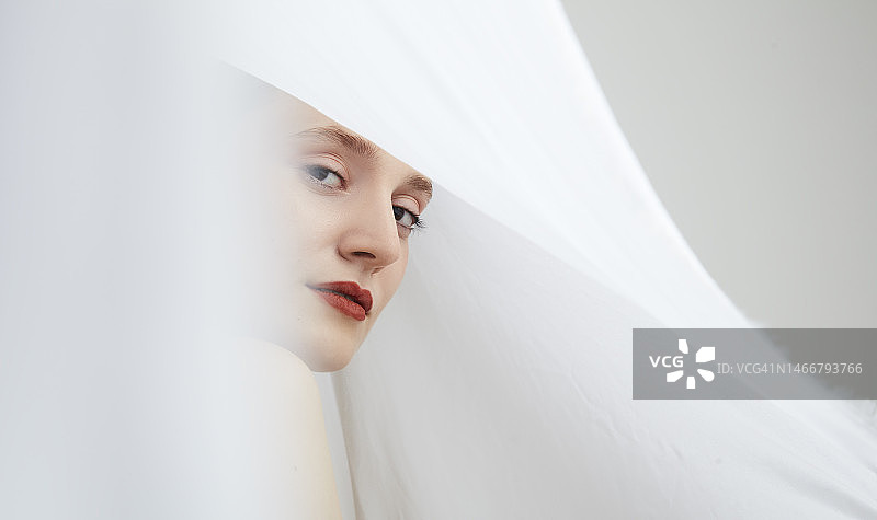 年轻女人透过飘逸白布望向镜头图片素材