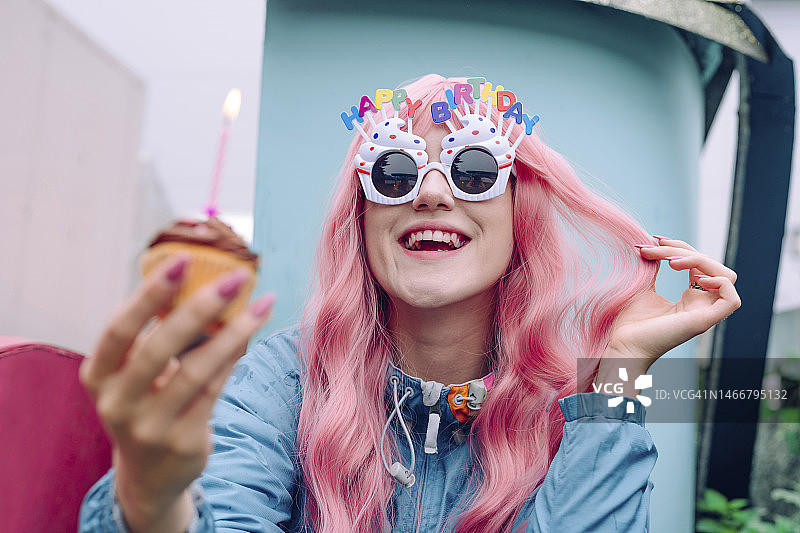 快乐的女人戴着新奇眼镜，拿着纸杯蛋糕庆祝生日图片素材