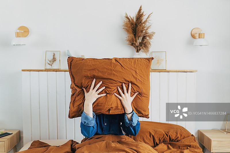 俯视独自在家用枕头捂住脸的沮丧女人，失眠、精神或人际关系问题、分手或离婚的年轻女性图片素材
