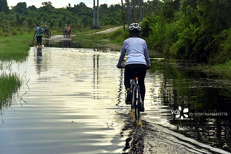 在被洪水淹没的道路上骑自行车的亚洲老年妇女图片素材