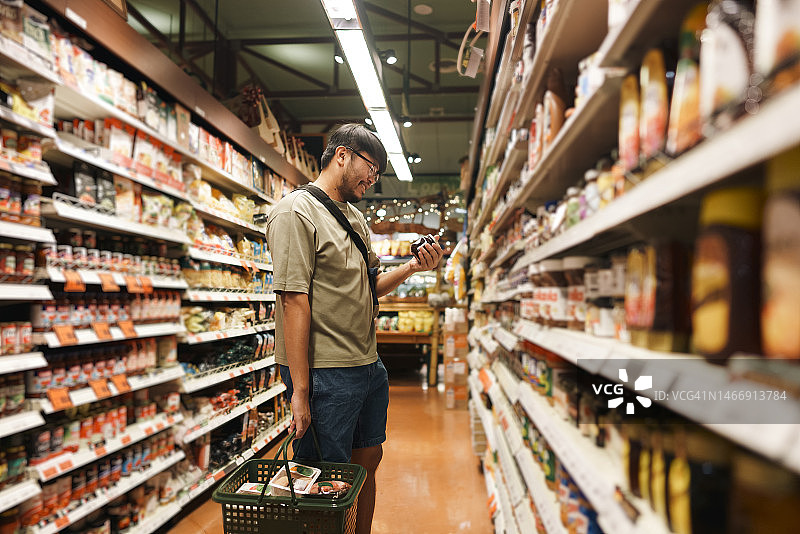 广角镜头：亚洲成年人在超市通道中携带购物篮并挑选商品图片素材