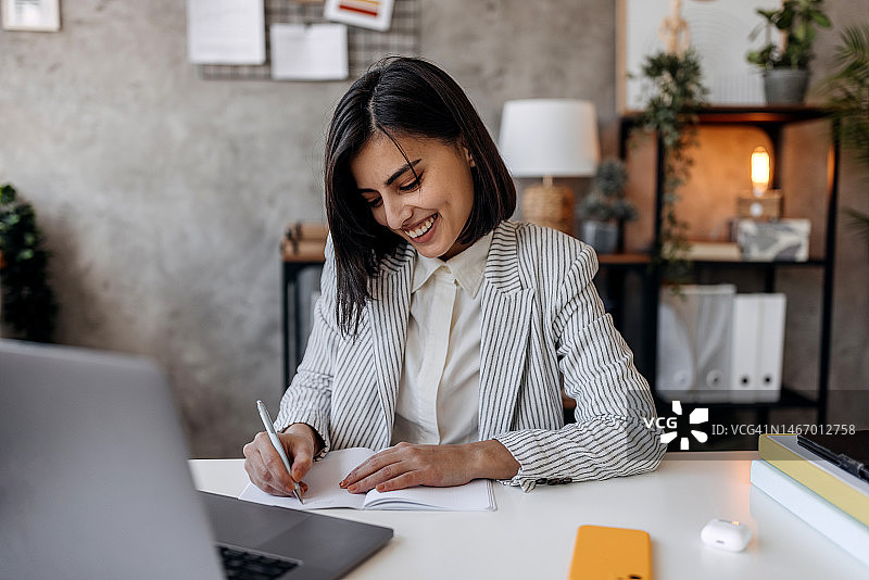 在家办公时微笑做笔记的年轻女商人图片素材