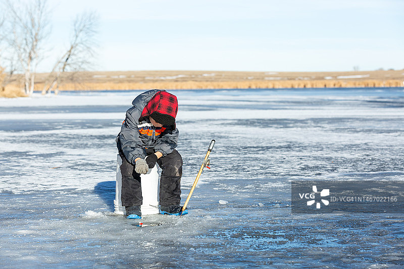 年轻男孩坐在桶上冰钓图片素材