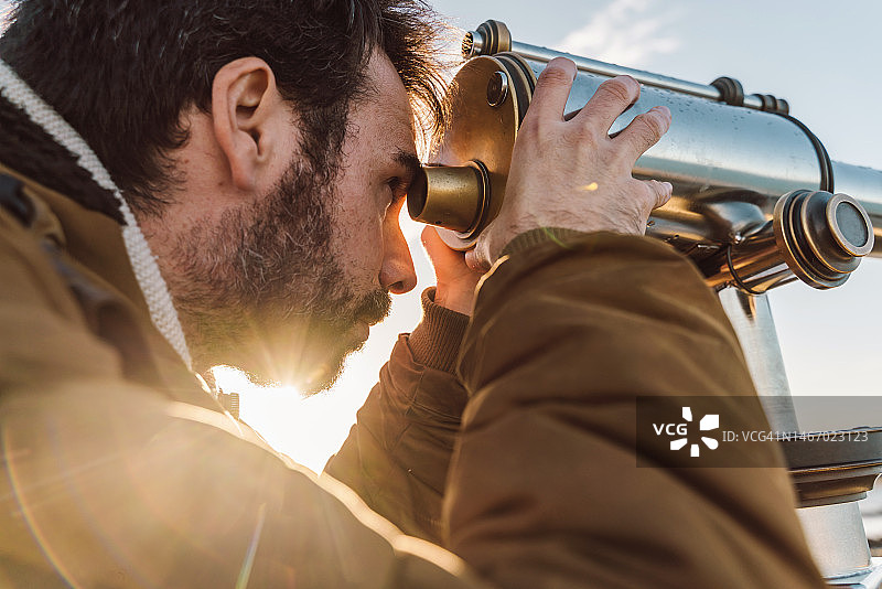 日落时分用望远镜眺望海滩地平线的白人旅行者图片素材
