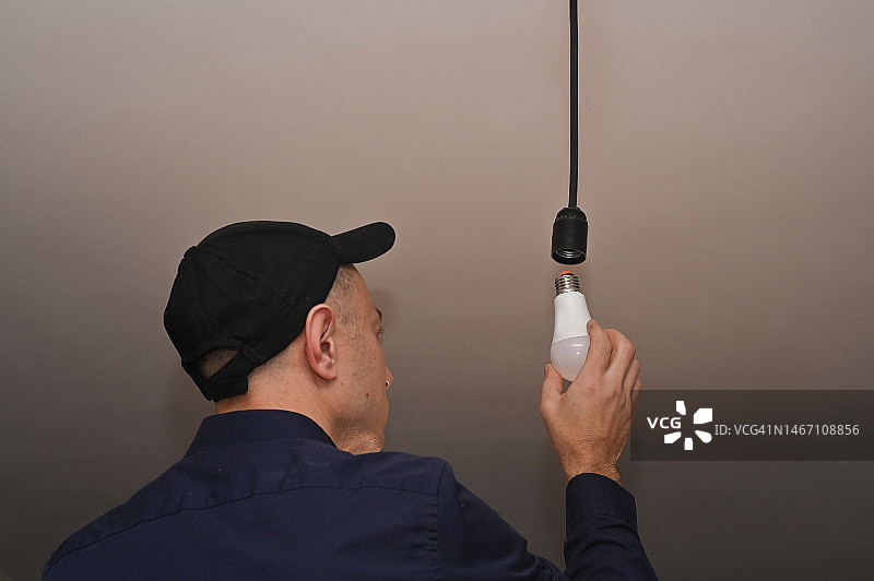 戴黑色工作帽的男人拧灯泡，安装LED灯图片素材