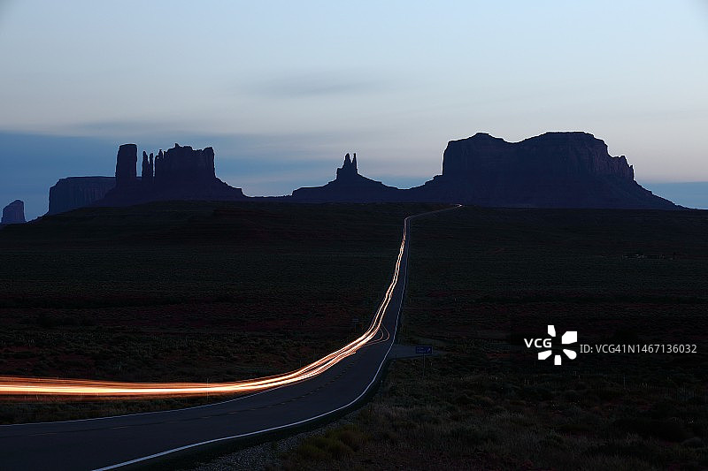 纪念碑谷岩石山丘剪影上汽车灯光的长曝光图片素材