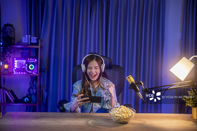 亚洲女孩在家用智能手机直播和玩手机游戏图片素材