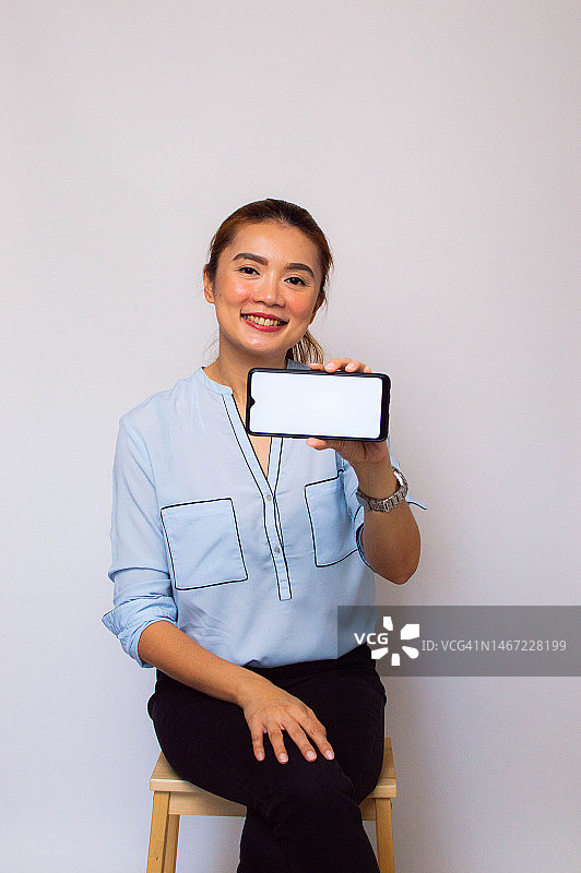 一位东南亚女子在白色背景上展示智能手机的设备屏幕图片素材