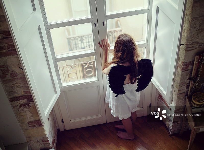 长着黑色天使翅膀、站在窗边向外看的少女图片素材