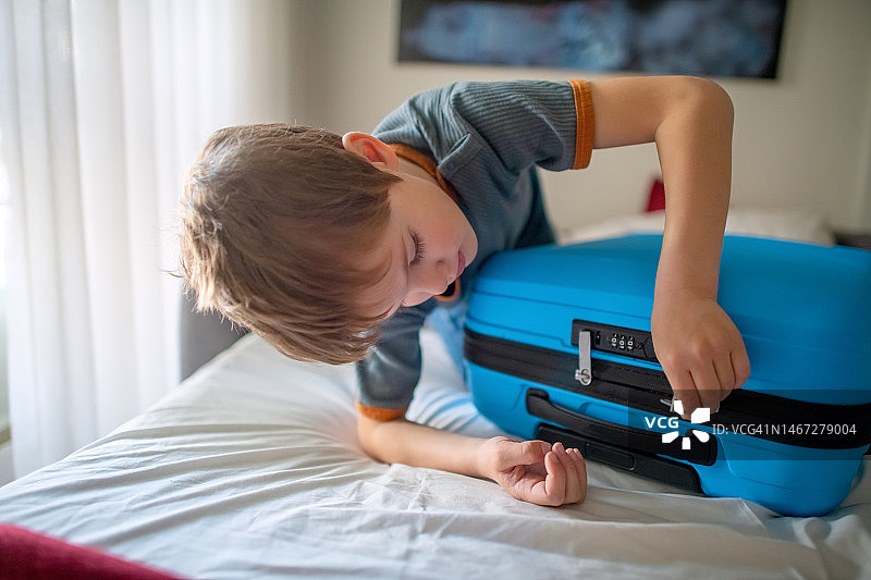 男孩在酒店房间或家中关闭并锁上手提箱，准备旅行图片素材