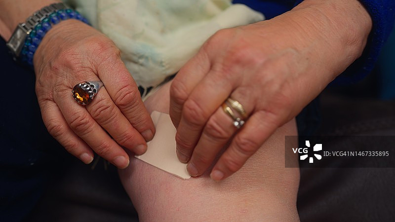 年长的女人在膝盖上贴止痛膏药图片素材