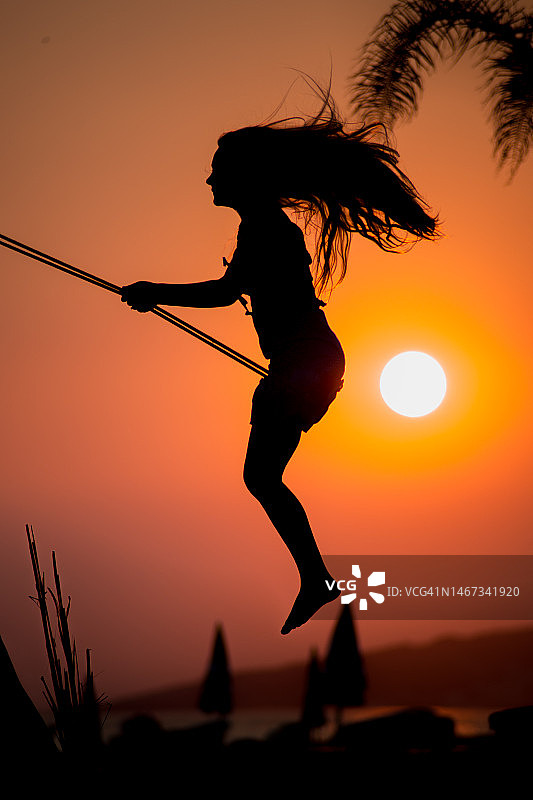 海滩上荡秋千的年轻女孩的剪影图片素材