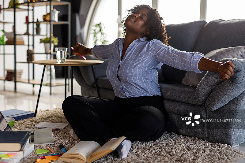 坐在地板上，伸展双臂同时学习的大学生图片素材