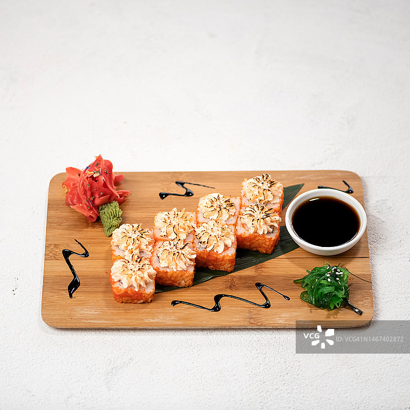 寿司卷套餐，竹叶木板上的奶油奶酪烤寿司卷，搭配酱油、姜、芥末、裙带菜，日式料理，白色背景，顶视图图片素材