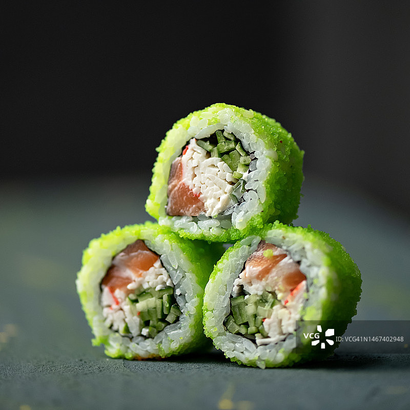 三份配绿色飞鱼籽的寿司卷。加州卷配鲑鱼、黄瓜和蟹肉。三个卷摆成金字塔形。日本食物。特写。侧视图。柔焦。复制空间图片素材