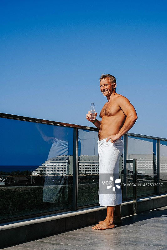 清晨阳台上，淋浴后喝水的微笑男人图片素材