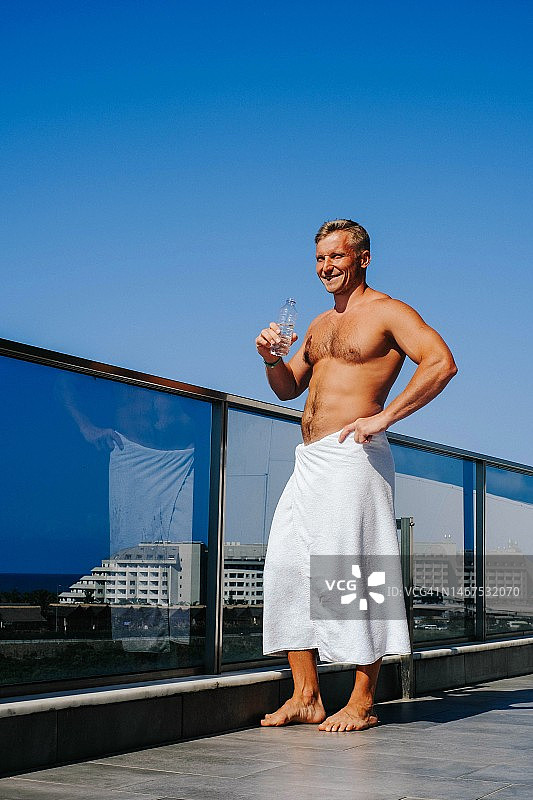 清晨阳台上，淋浴后喝水的微笑男人图片素材