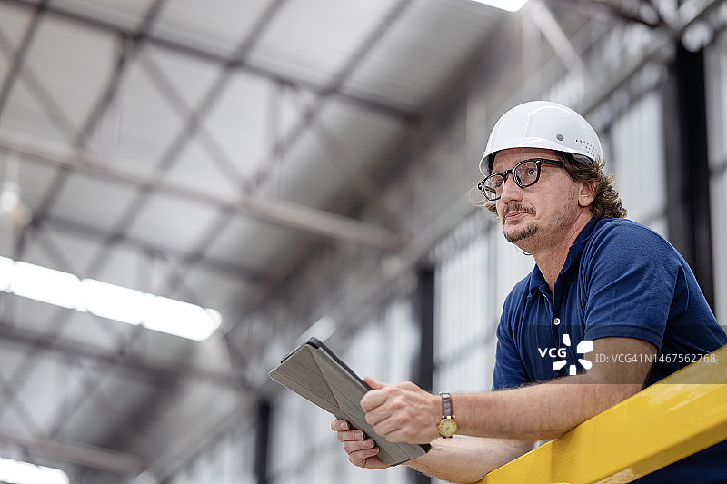 使用精益六西格玛优化制造业效率。一名商务人士用平板电脑盯着生产线车间的低角度视图。图片素材