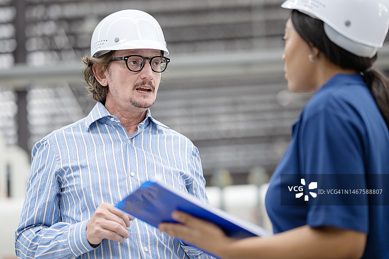 制造运营中团队成员之间进行有效沟通的双向沟通方法。工厂经理与非裔美国女工程师讨论，跟进工厂车间的生产计划。图片素材