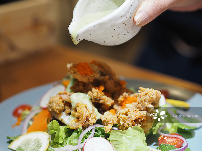 女人手持杯子，将酱汁淋在香辣蔬菜沙拉炸鱿鱼上图片素材