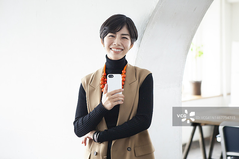 在办公室拿着手机微笑的年轻女商人肖像图片素材