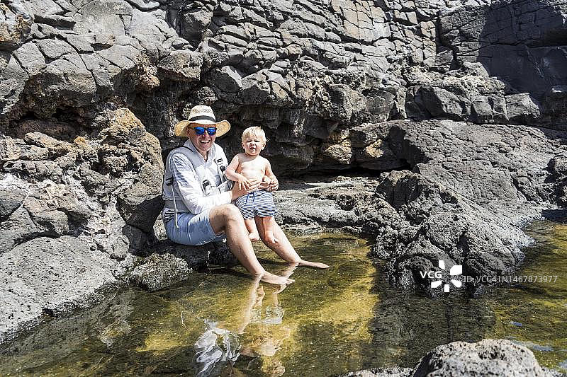 在西班牙兰萨罗特岛，父亲和小儿子在天然水池里玩水图片素材