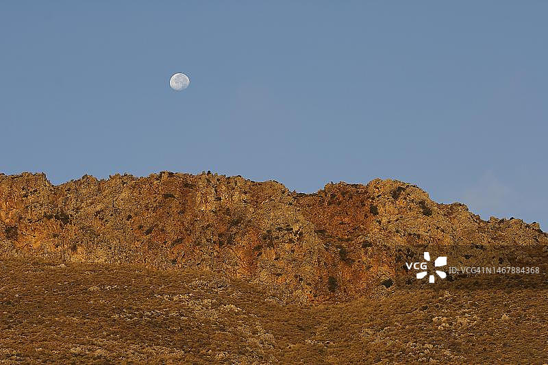 金色晨光：覆盖在山脉上的月亮，位于希腊克里特岛格拉姆武萨半岛海盗湾巴洛斯图片素材