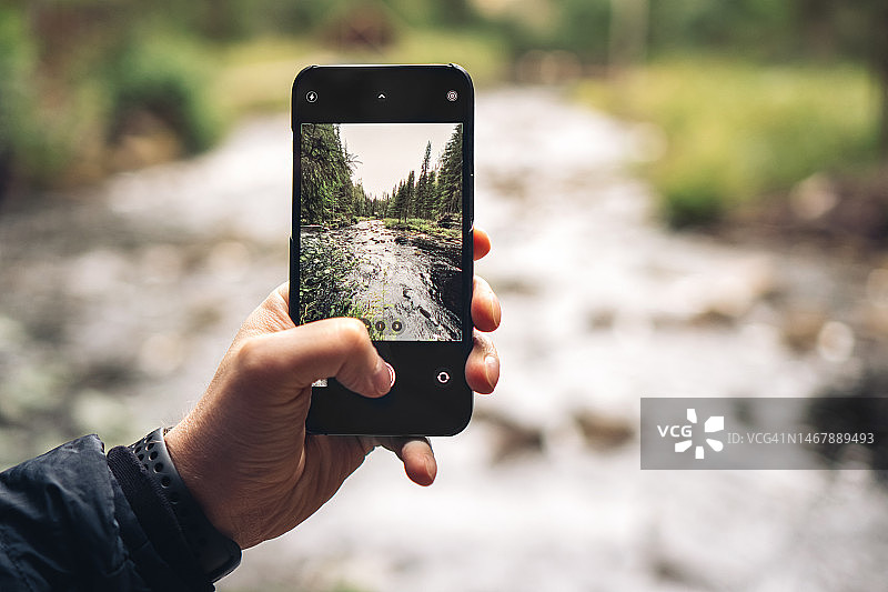 男人手持手机拍摄瀑布。旅行、科技、自然、正念概念图片素材
