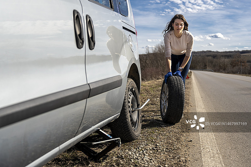 在路上更换汽车轮胎的年轻女子图片素材