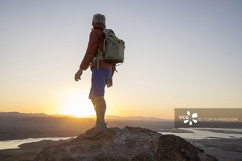 年长的徒步旅行者在日落时分停留在山顶，俯瞰湖面图片素材