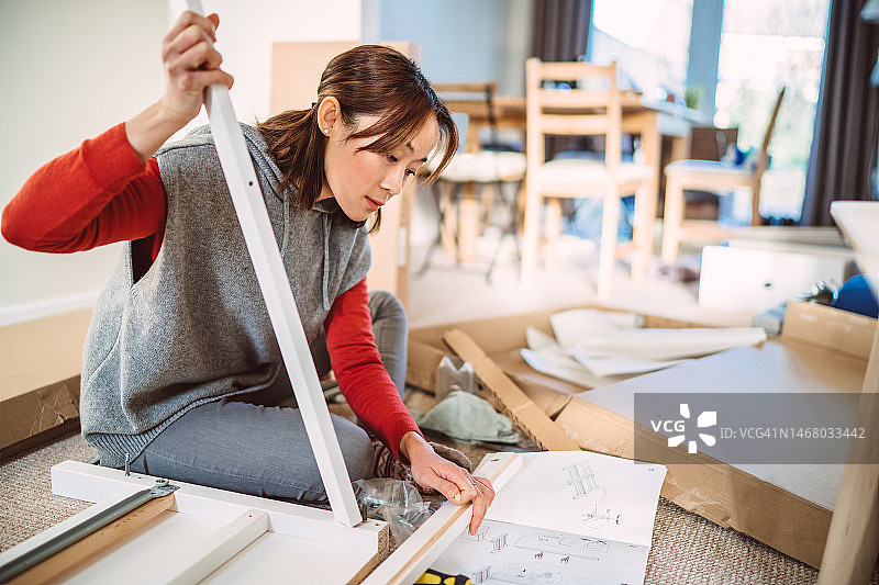 年轻漂亮女人在新家组装家具时阅读说明书图片素材