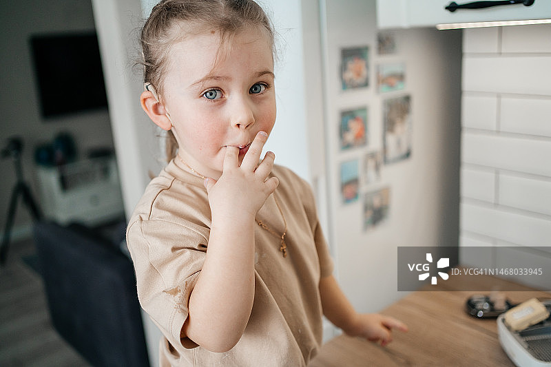 在厨房里舔手指的植入人工耳蜗的儿童图片素材