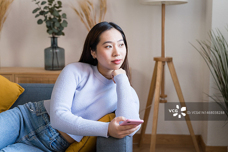 身穿休闲装的年轻亚洲女子在沙发上休息微笑看向镜头图片素材