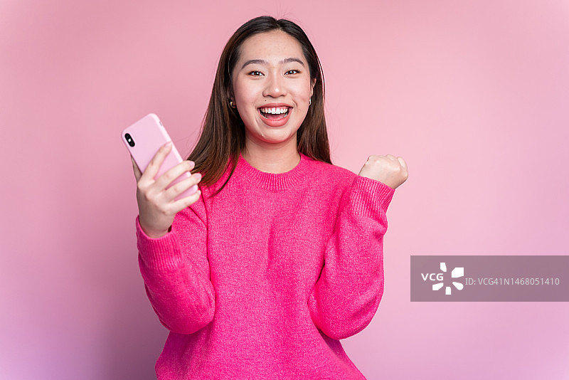 微笑的亚洲女人用智能手机庆祝好消息图片素材