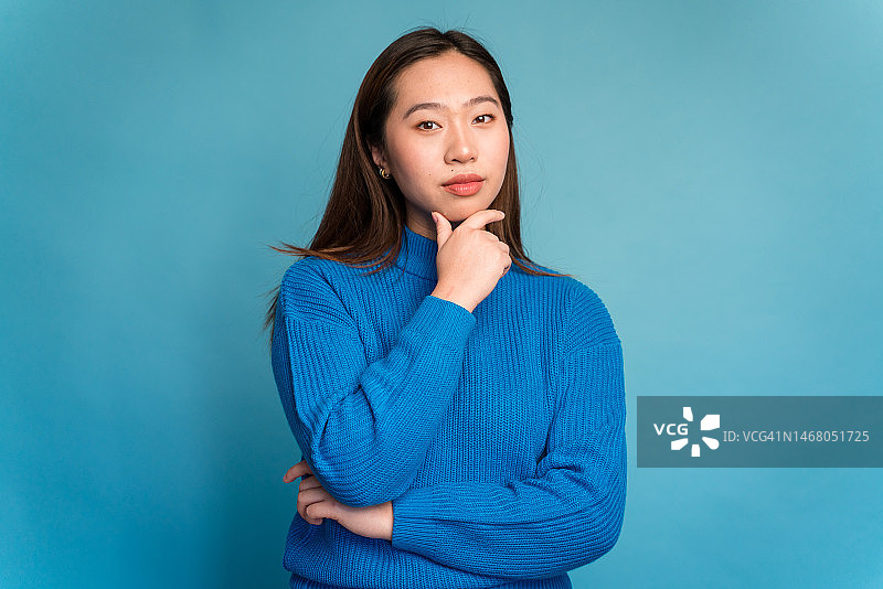 年轻女人摸着下巴看着镜头，做出思考的手势图片素材