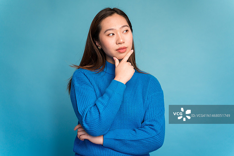 年轻女人摸着下巴看着镜头，做出思考的手势图片素材