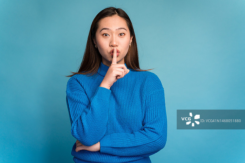 演播室里手指放在嘴唇上看着镜头的年轻女子，表示安静图片素材