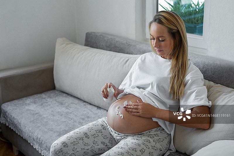 年轻孕妇在腹部涂抹润肤霜图片素材