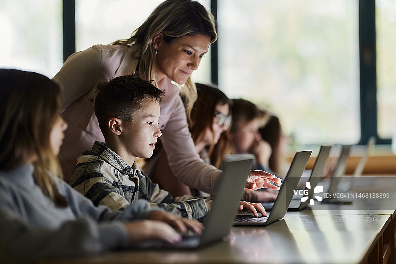 女教师在课堂上帮助小学生使用电脑图片素材