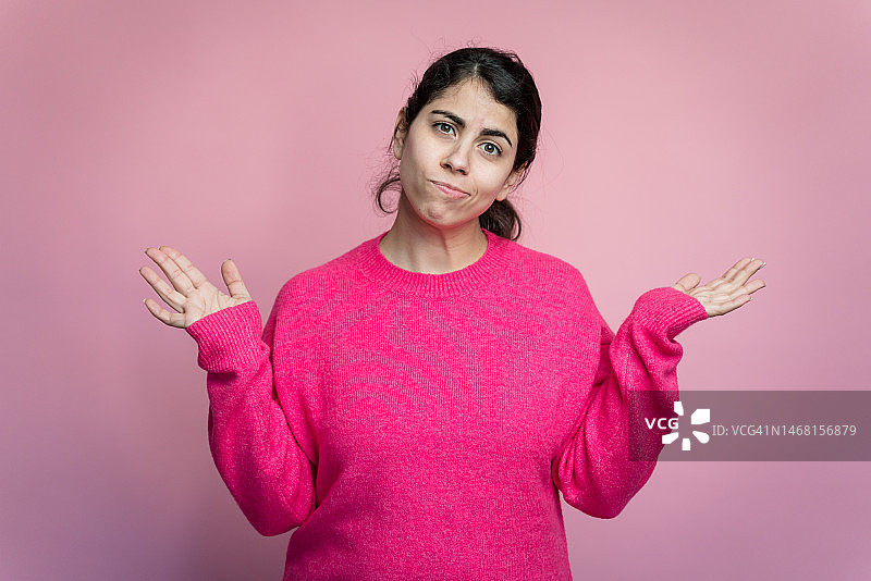演播室粉色背景下穿粉色毛衣，表情茫然的女人图片素材