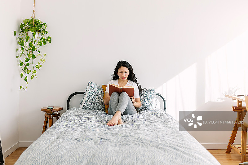 早上坐在床上看书的年轻千禧一代女学生图片素材